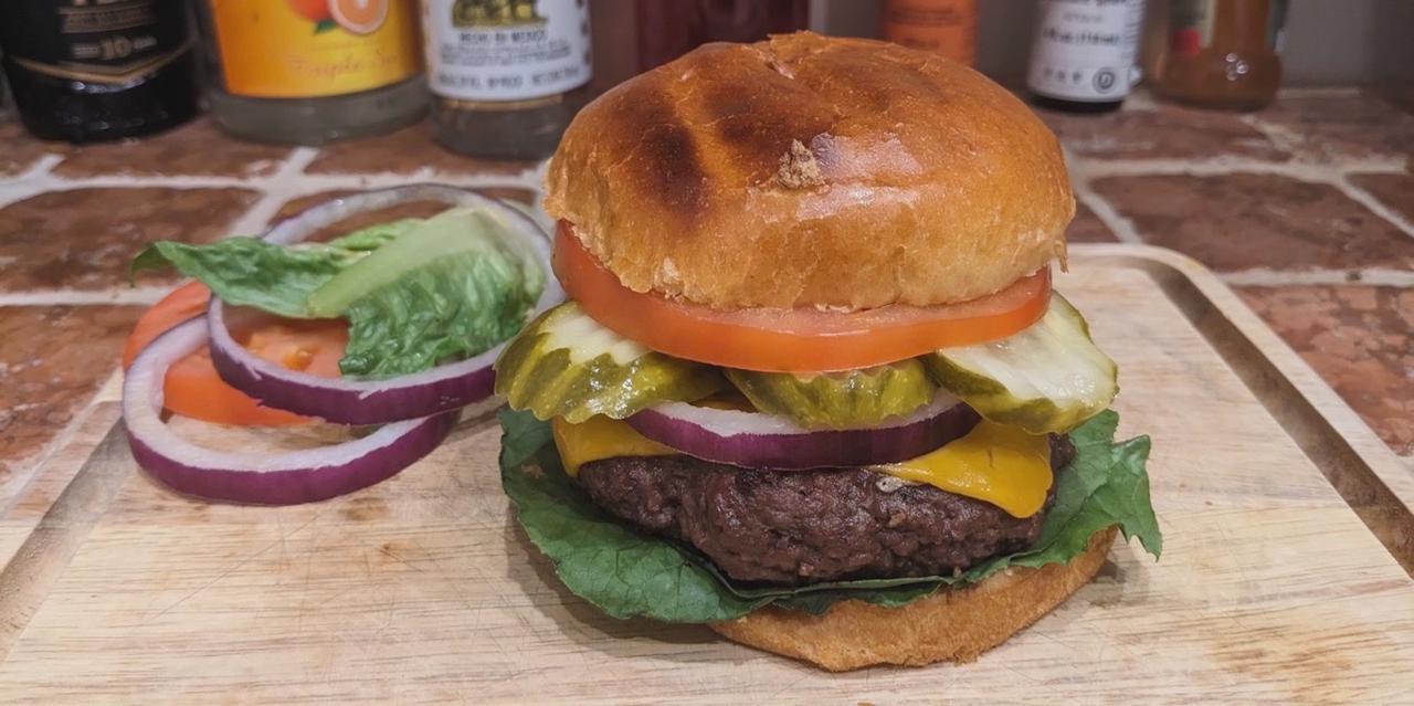 A Cheeseburger with lettuce, tomato, onion, pickle.