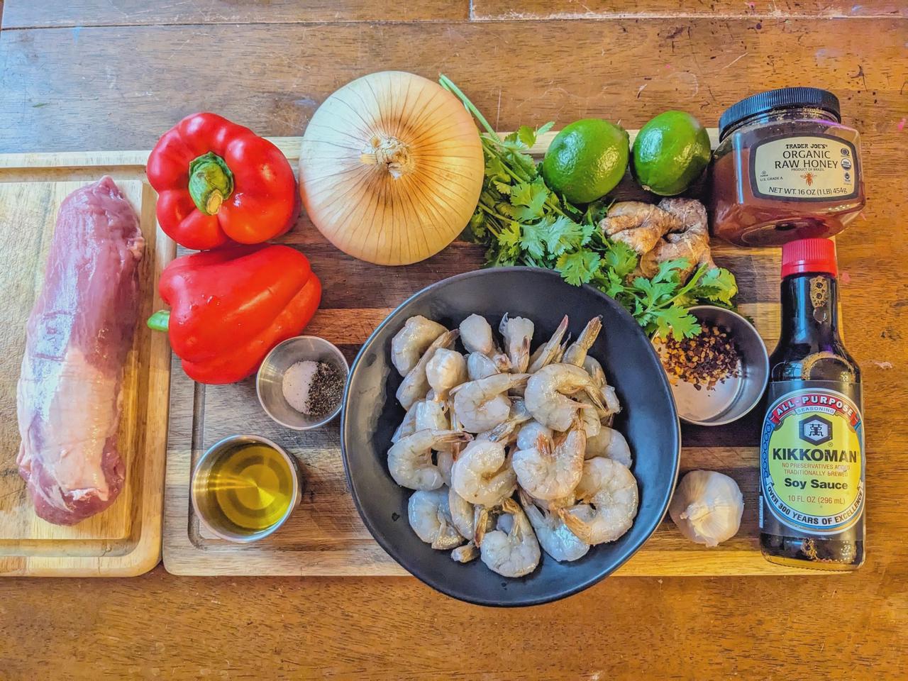 Platter of ingredients for pork and shrimp skewers on a wood cutting board.