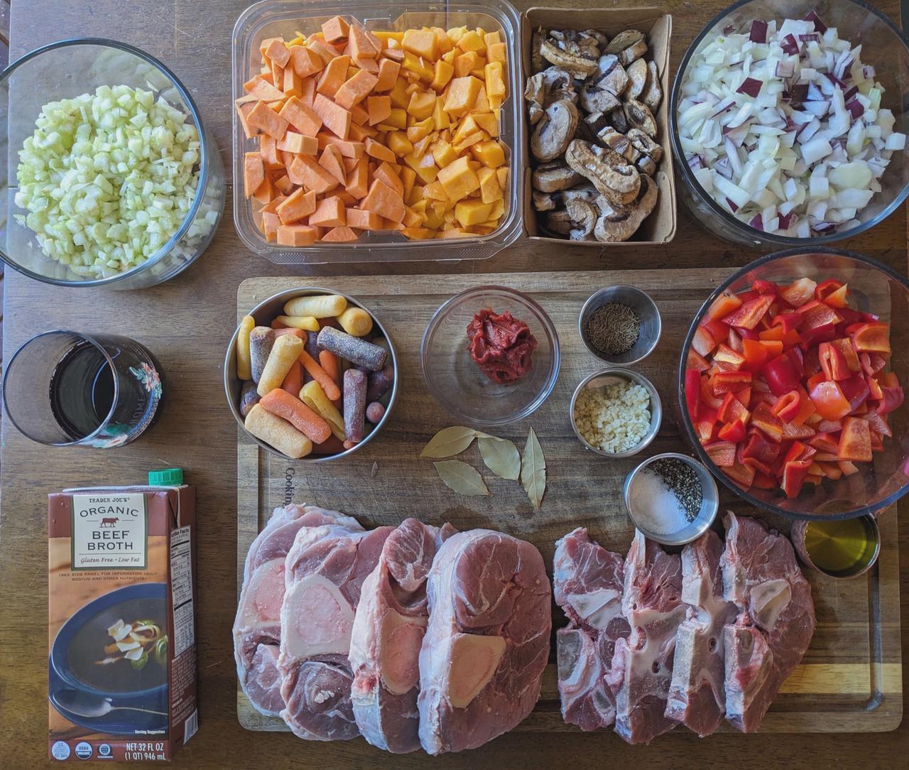 Platter of ingredients for beef shank and neck stew on a wood cutting board.