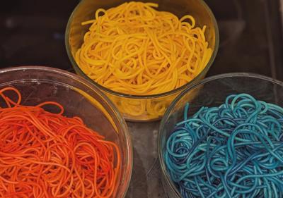 Three bowls of colorful spaghetti in shades of red, yellow, and blue