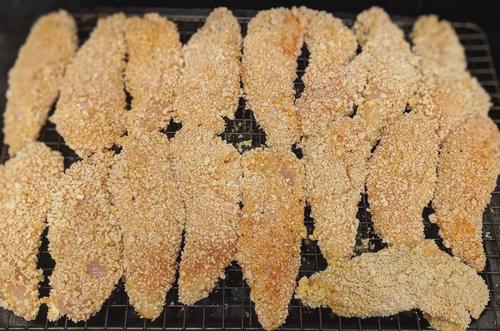 Uncooked chicken tenders coated in flour, egg, and breadcrumbs.