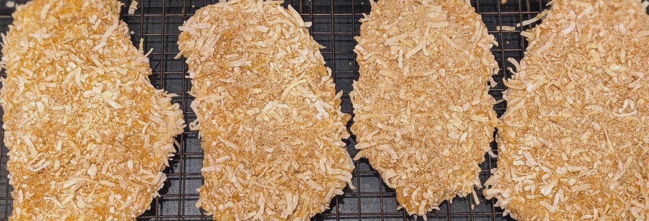 Uncooked, coconut-breaded chicken cutlets on a wire rack and baking sheet.