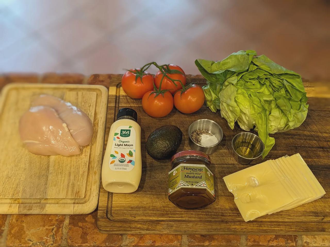 Platter of ingredients for Grilled Chicken and Avocado Sandwich with Honey-Mustard Spread on a cutting board.