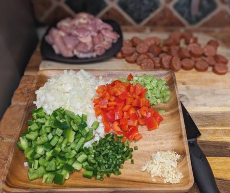 A platter of diced “Holy Trinity” vegetables—onion, bell pepper, and celery—alongside minced garlic, ready to be sautéed in the roux for the Korean Gumbo. The vibrant colors and textures of the vegetables promise a flavorful and aromatic base for the dish.