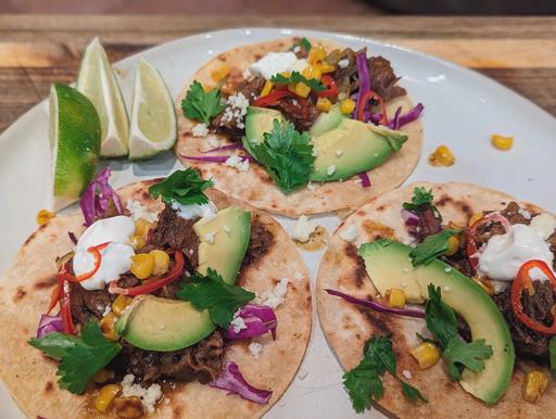 Close-up of Mississippi Pot Roast Tacos, showing the juicy shredded beef, creamy avocado, and charred corn wrapped in soft tortillas.