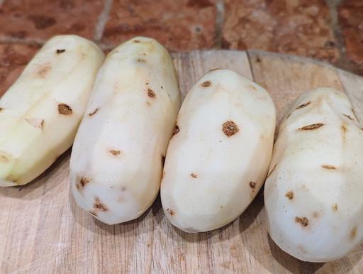 Peeled potatoes on a cutting board.